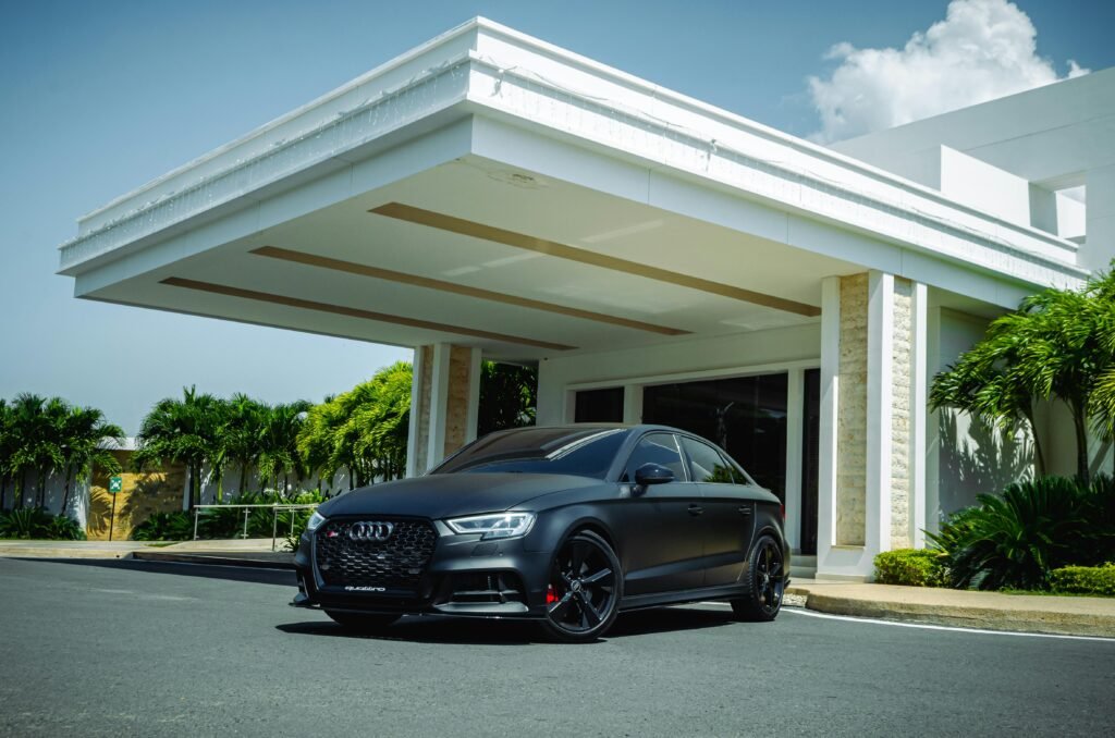 pexels-photo-19805726-19805726 A sleek black Audi RS3 sports car parked in front of a modern building with clear blue skies and lush greenery.