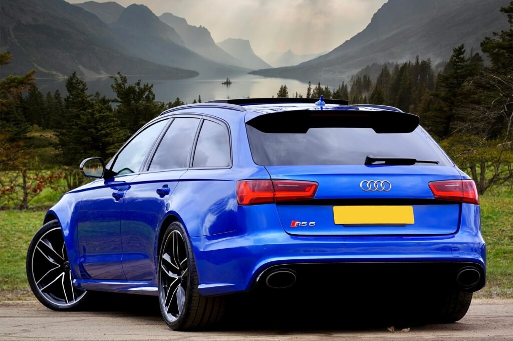 A sleek blue Audi RS 6 wagon parked against a stunning backdrop of Scottish hills and a serene lake.