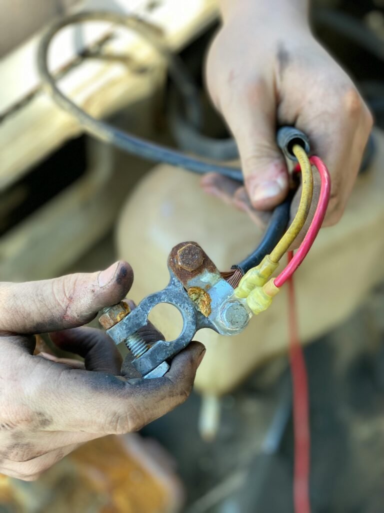 Hands holding a corroded battery terminal with multi-colored wires in a repair setting.