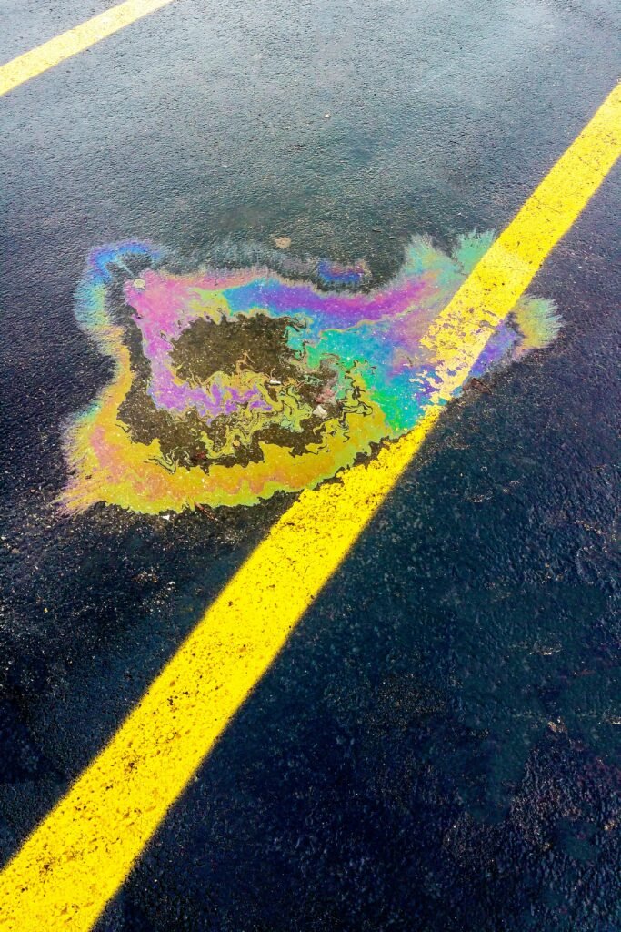 Vibrant rainbow-colored oil spill on black asphalt with yellow lines in a parking lot.