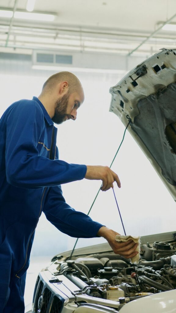 Mechanic inspecting car engine oil with dipstick in an automotive repair shop.